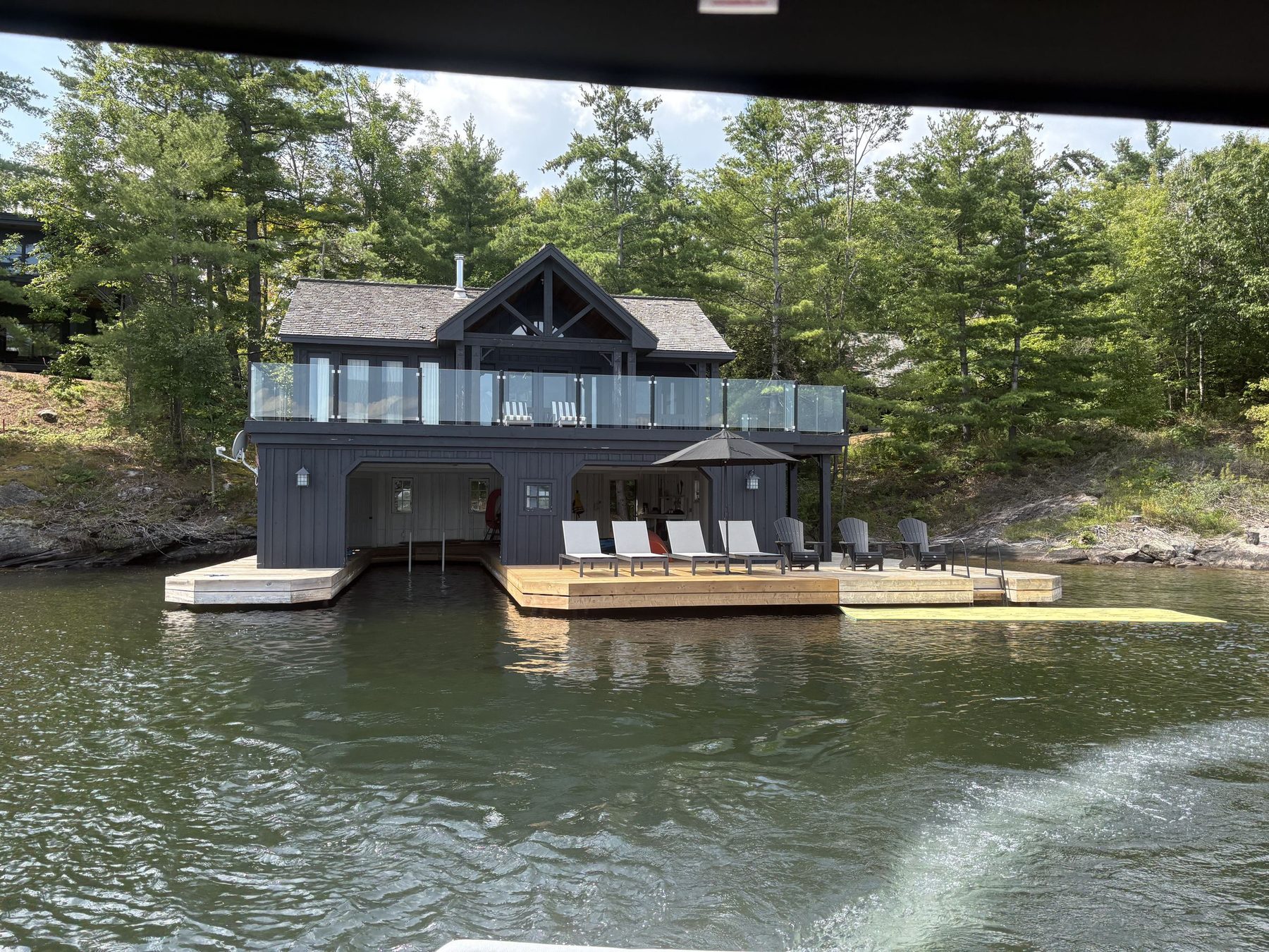 The charcoal boathouse from the water, glass-railed deck and two slips
