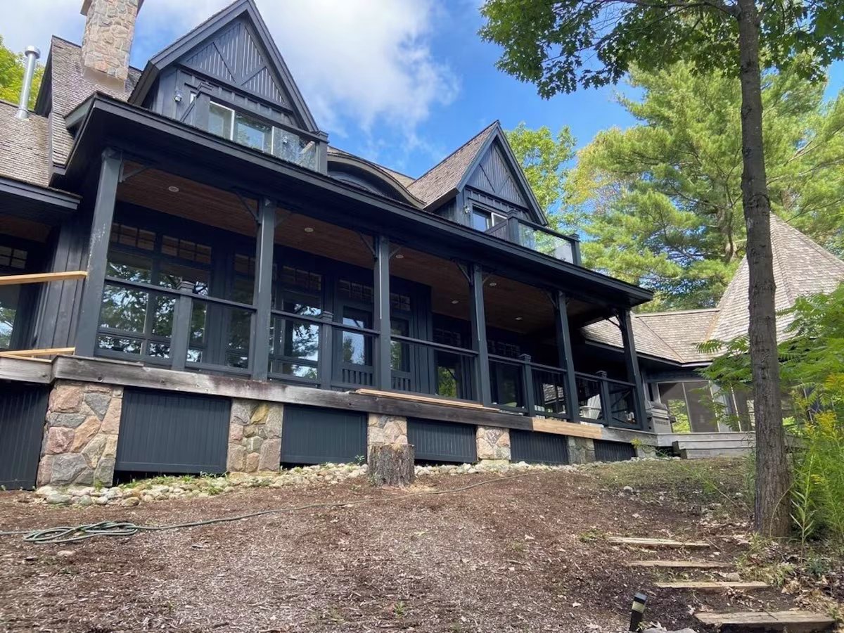 Lakeside elevation of the cottage — covered porch, stone foundation, and cedar-shingle roof