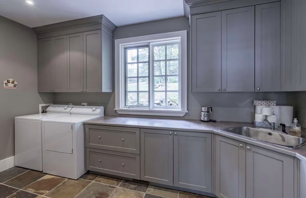 Laundry room with grey cabinetry, a deep sink, and a window onto the granite
